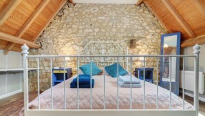 A bed with a metal frame, a stone wall, and wooden beams in a room.