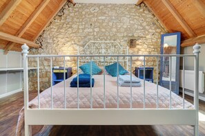 A bed with a metal frame, a stone wall, and wooden beams in a room.