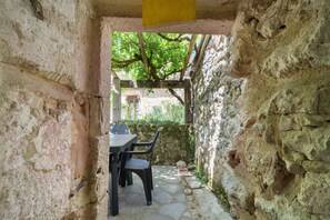 A stone-walled outdoor seating area with a table and chairs, a wooden pergola, and a view of greenery and a building in the background. - Holiday Home “Cottage Blanc” with Private Terrace and Wi-Fi (Beaumontois en Périgord)