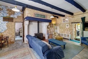 A rustic room with exposed stone walls, a blue sofa, a wooden bench, and a dining table.