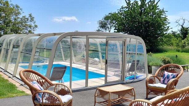 Ein überdachter Außenbereich mit Pool, Korbmöbeln und einer Glaseinfriedung.