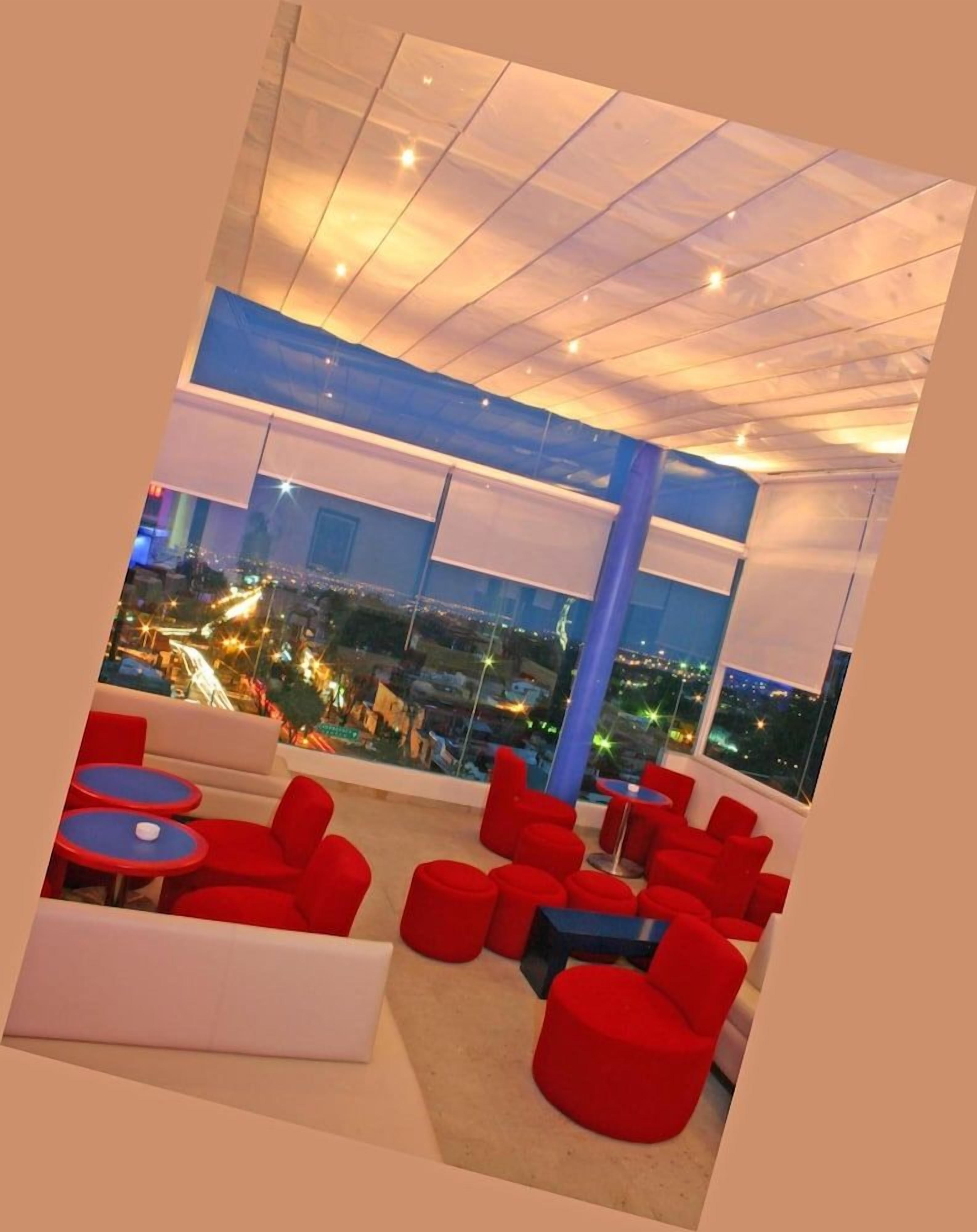 Un salón en la azotea con asientos rojos y vistas a la ciudad.