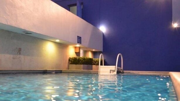 A swimming pool with clear water, a pool ladder, and a wall with a light fixture.