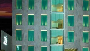 A multi-story hotel with a modern design, featuring a grid of windows and a central glass elevator shaft.