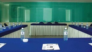 A conference room with a long table, chairs, water bottles, and a projector screen.
