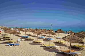 Uma praia com fileiras de espreguiçadeiras e guarda-sóis de palha.