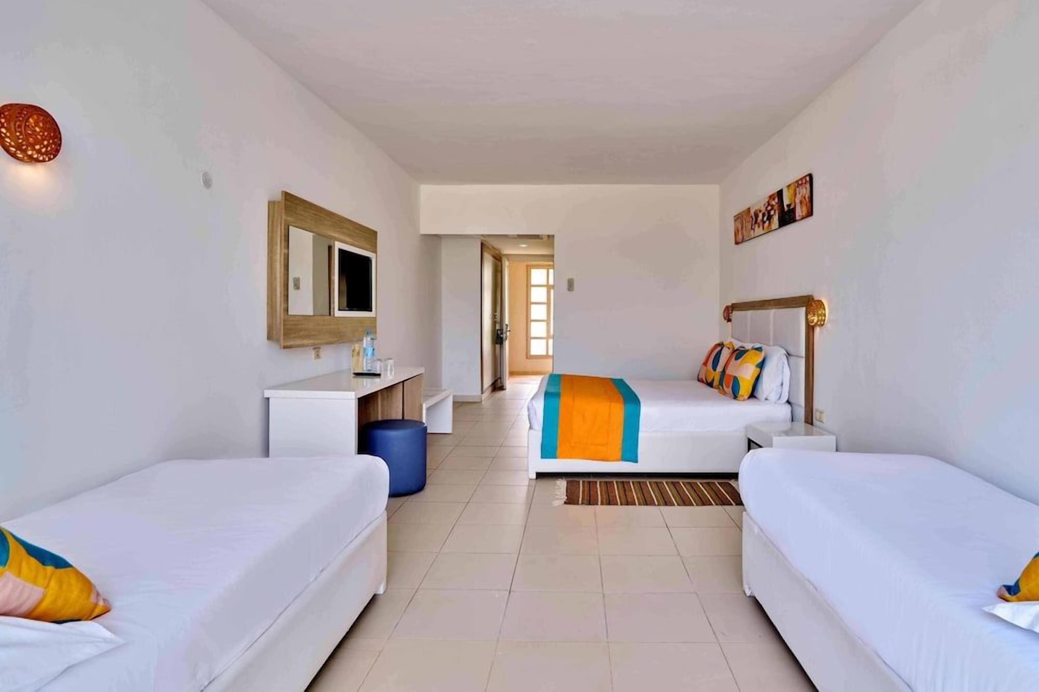 A hotel room with two single beds, a desk, a chair, a mirror, and a view of the hallway.