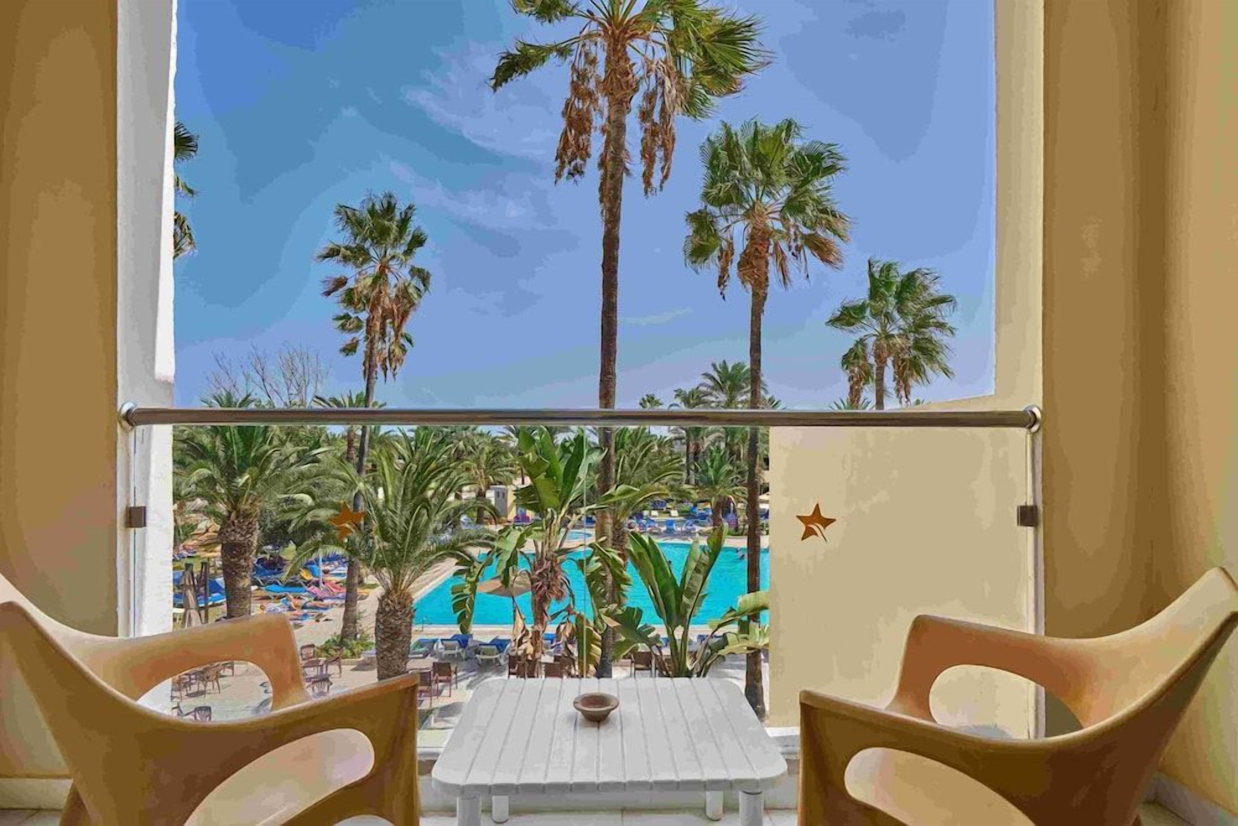 A balcony with a view of a pool and palm trees.