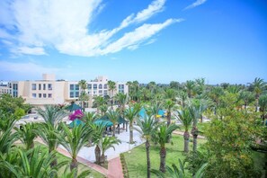 A hotel courtyard with palm trees, a pool, and a building with multiple windows. - Palm Beach Skanes (Monastir)