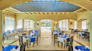 Un vaste espace dédié à la salle à manger, avec des tables disposées pour accueillir de nombreux convives, un grand plafond en arc de cercle et une lumière naturelle provenant des fenêtres.