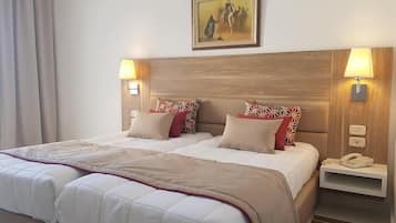A hotel room with a large bed, two bedside tables, a painting on the wall, and a lamp on each table.