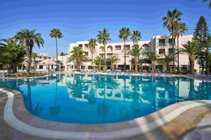 Um hotel com uma piscina grande, rodeada por palmeiras e espreguiçadeiras.