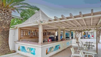 Uma área de bar ao ar livre com um espaço de estar coberto, balcão com cardápio e vista para a piscina.