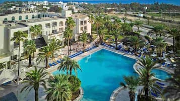 A resort with a central swimming pool surrounded by palm trees and lounge chairs.