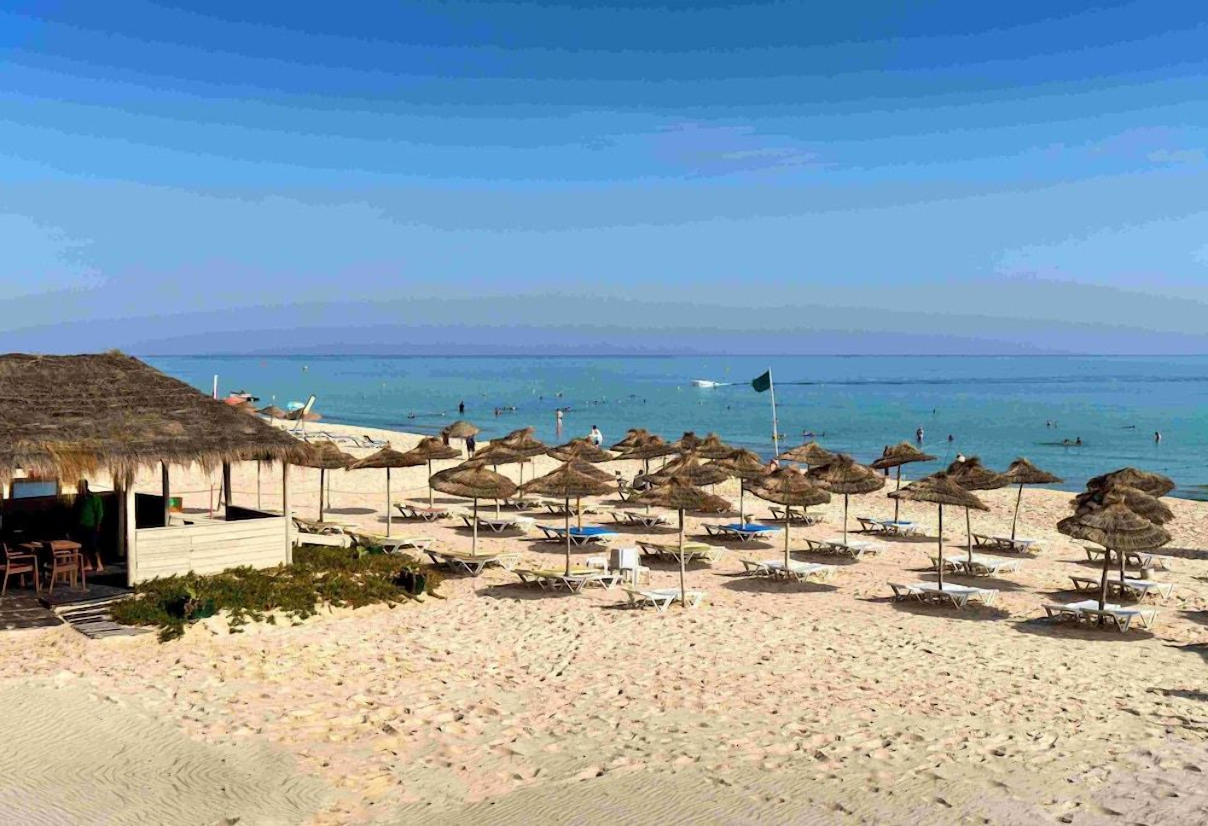 A beach with thatched umbrellas and lounge chairs, a wooden structure, and the ocean in the background.