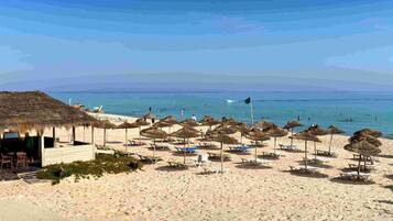 A beach with thatched umbrellas and lounge chairs, a wooden structure, and the ocean in the background.