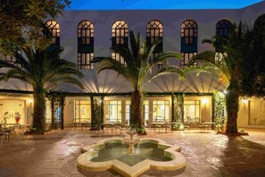 A courtyard with a fountain, palm trees, and a building with arched windows. - Palm Beach Skanes (Monastir)
