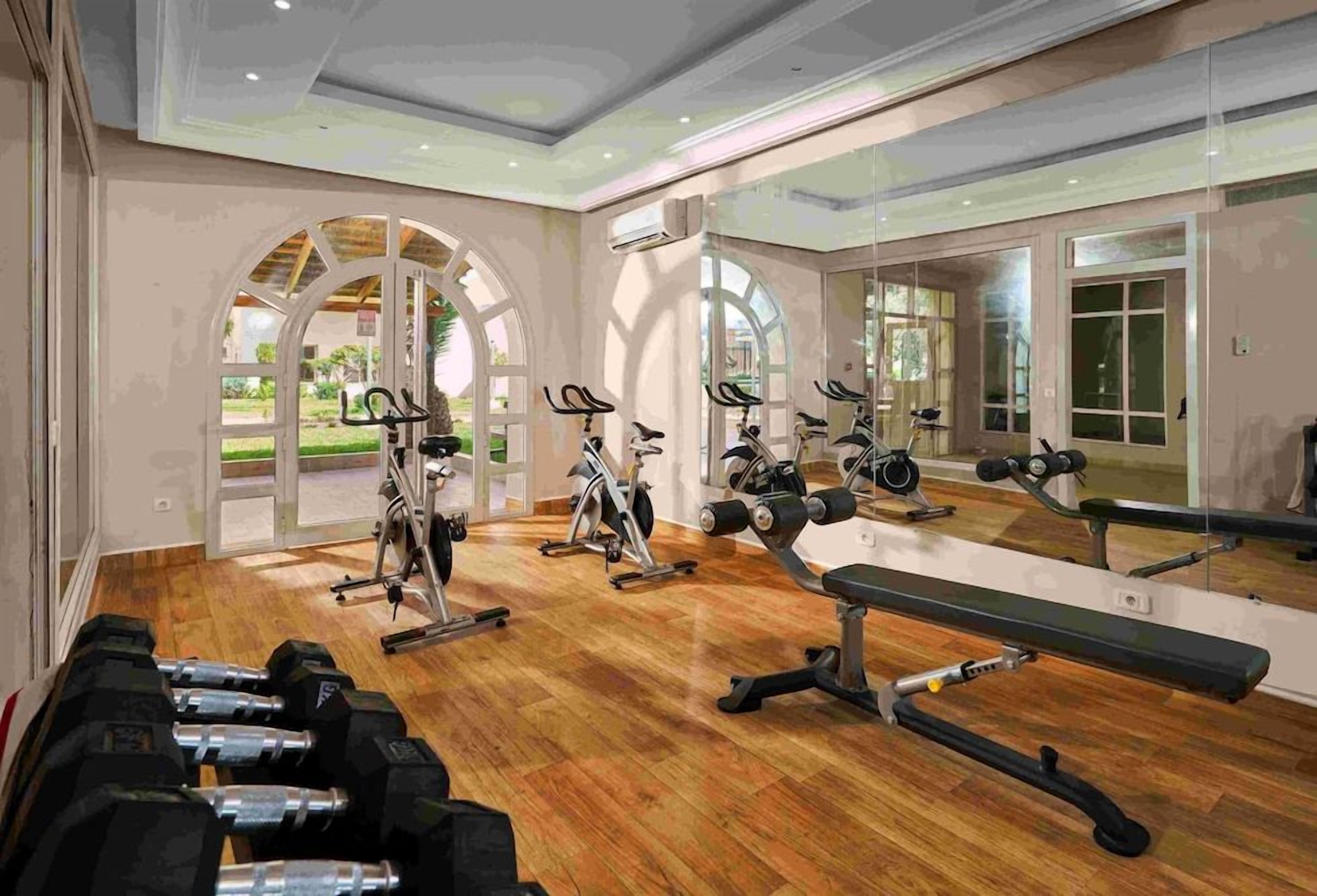 A gym with exercise equipment, a bench, and a large mirror reflecting the space.