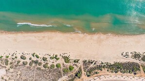 Ett flygbildsbild av en strand med kristallklart turkosfärgat vatten, en sandstrand och sparsam växtlighet.
