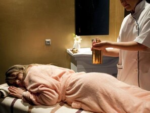 Una persona recostada en una camilla recibiendo un tratamiento, con un terapeuta de masaje a su lado.