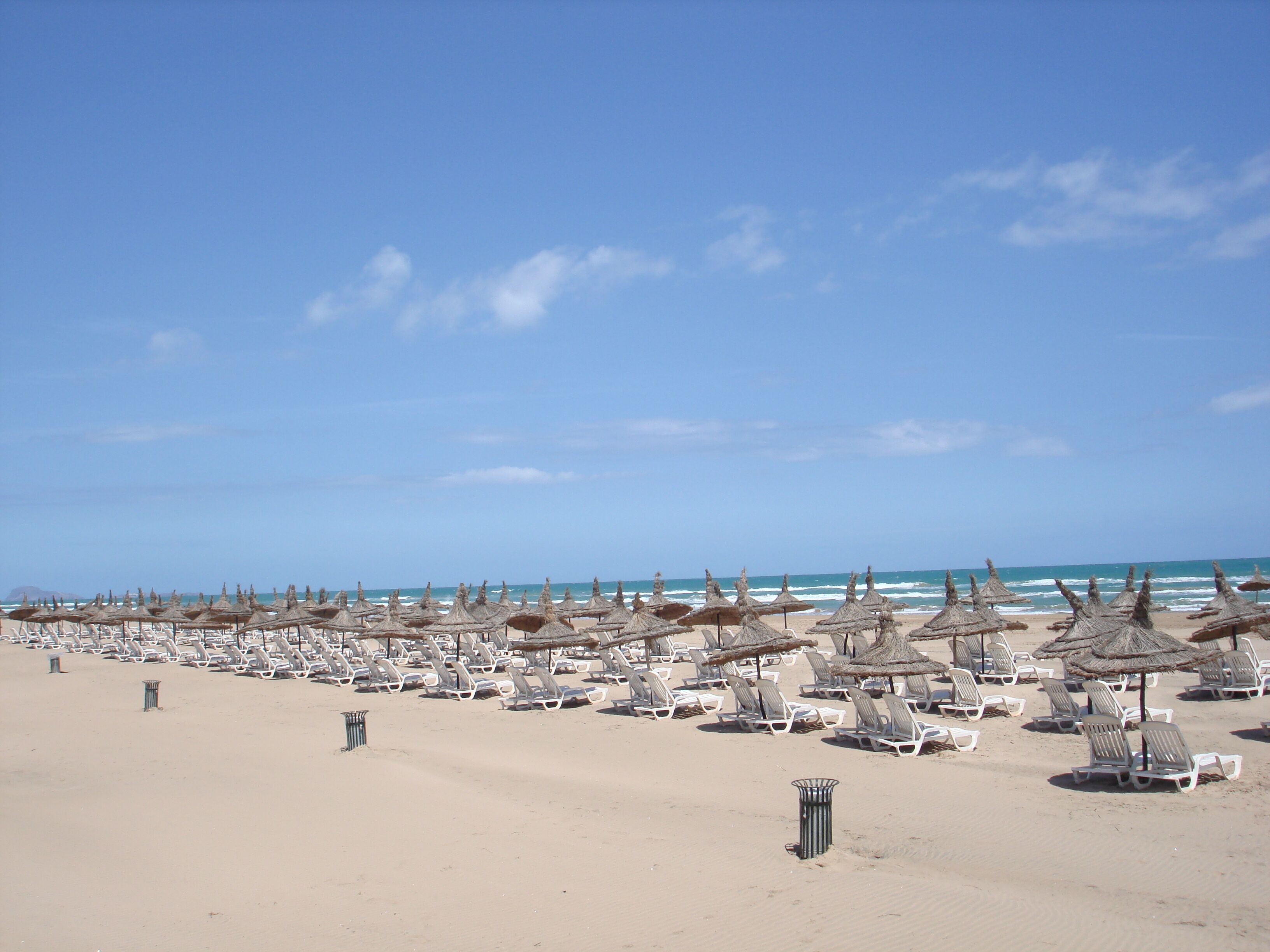 Ein Strand mit Reihen von Liegestühlen und Reetsonnenhüten.