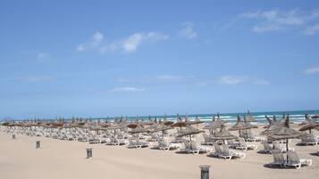 A beach with rows of sun loungers and thatched umbrellas.