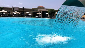 En swimmingpool med kristallklart blått vatten, solstolar och parasoller.