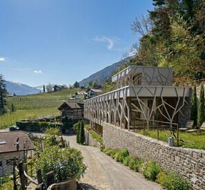 En moderne bygning med en geometrisk facade, en stenvæg og en sti, der fører hen til et traditionelt hus.