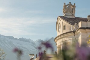 A building with classical architecture, a statue on the roof, and snow-covered mountains in the background. - Ladder Living Apartment in panoramic location (Algund)