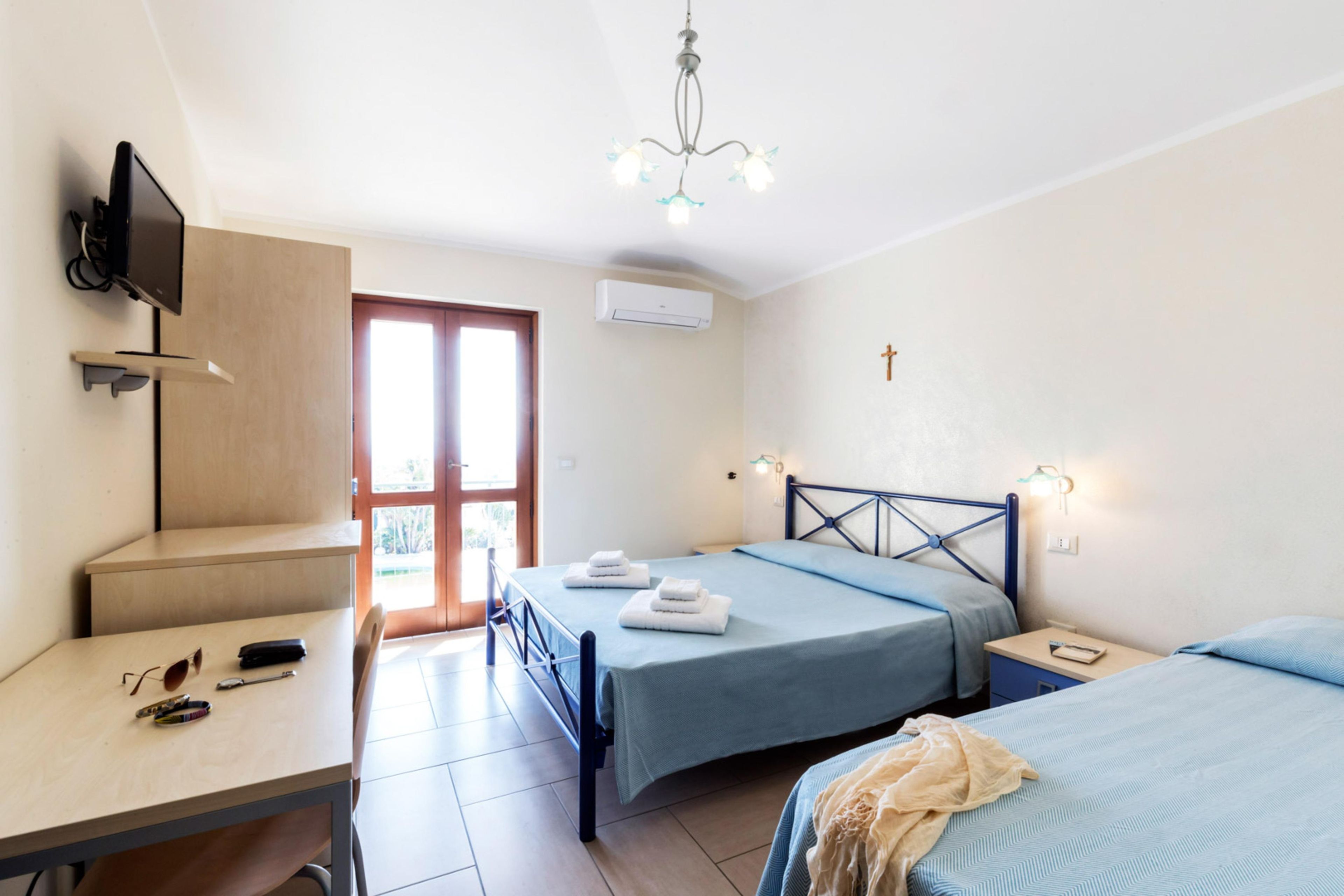 Una camera da letto con due letti, una scrivania, un televisore e un lampadario.