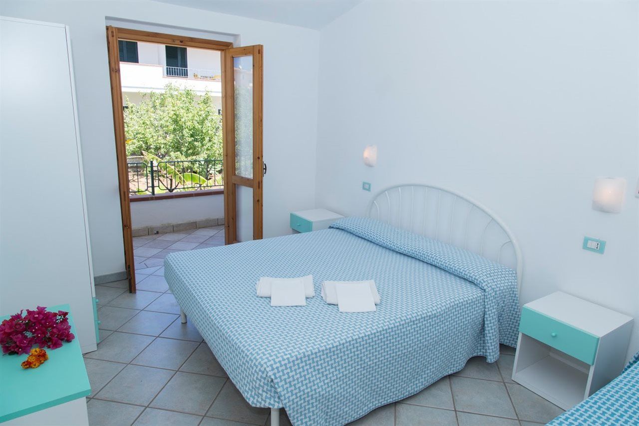 A bedroom with a bed, bedside tables, a window, and a view of a balcony.