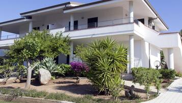 Un edificio a due piani con tetto piatto, diversi balconi e un giardino curato con varie piante.