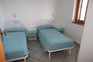 Una habitación pequeña y limpia con dos camas individuales, cada una con cabecera y piecera a juego, y una ventana con marco de madera.