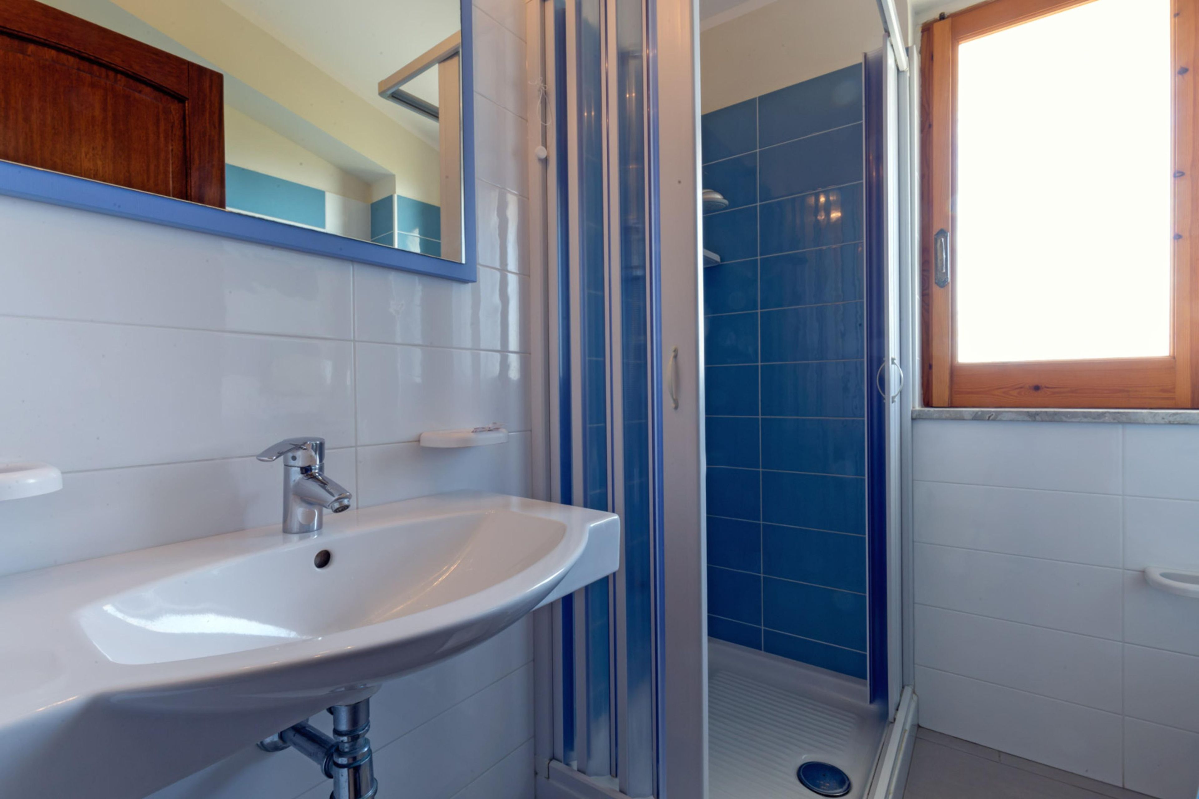 A bathroom with a white sink, a mirror, and a shower area with blue tiles.