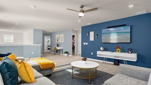 A modern living room with a blue accent wall, a round coffee table, and a flat-screen TV mounted above a white console. - King Ensuite Private Bath Shared Home (Davenport)