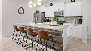 A modern kitchen with white cabinetry, a central island with stools, a stainless steel refrigerator, and a microwave. - King Ensuite Private Bath Shared Home (Davenport)