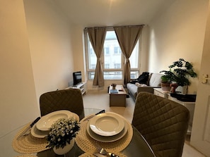 A dining area with a table set for two, a sofa, a coffee table, and a view of the city through large windows. - Bristol City Centre Apartment, Marsh Street (Bristol)