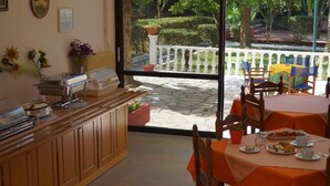 Zona de petit esmorzar amb un sistema de menjar a voluntat, seients a l'exterior amb tovallons taronja i vista a un jardí a través d'una porta de vidre.
