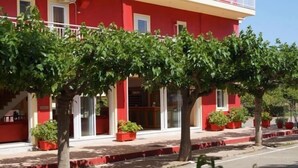 Un edifici vermell amb un vestíbul cobert, plantes en testos i un cel serè.