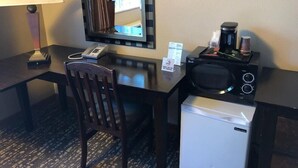 A hotel room with a desk, chair, lamp, microwave, coffee maker, and a mini fridge. - District Hotel (Portland)
