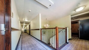 A long hallway with patterned carpet, a wooden door on the left, and a staircase with a metal railing on the right. - District Hotel (Portland)