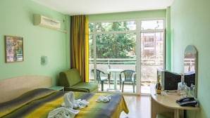 A hotel room with a bed, a desk with a computer, a chair, a table with chairs, and a window with a view of greenery and buildings. - Hotel Dalis (Nessebar)