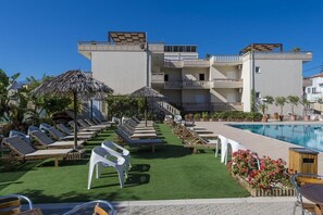Un hotel con piscina, tumbonas y una sombrilla de paja.