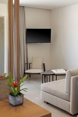 Una sala de estar moderna con un televisor de pantalla plana montado en la pared, un sofá, un sillón y una mesita con un libro.