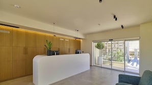 Un área de recepción con un mostrador blanco, armarios de madera, una planta en maceta y una silla azul.