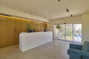 Un área de recepción con un mostrador blanco, armarios de madera, una planta en maceta y una silla azul.