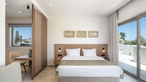 Una habitación de hotel moderna con una cama grande, lámparas de noche, vistas a la ciudad y un comedor con una mesa y sillas.