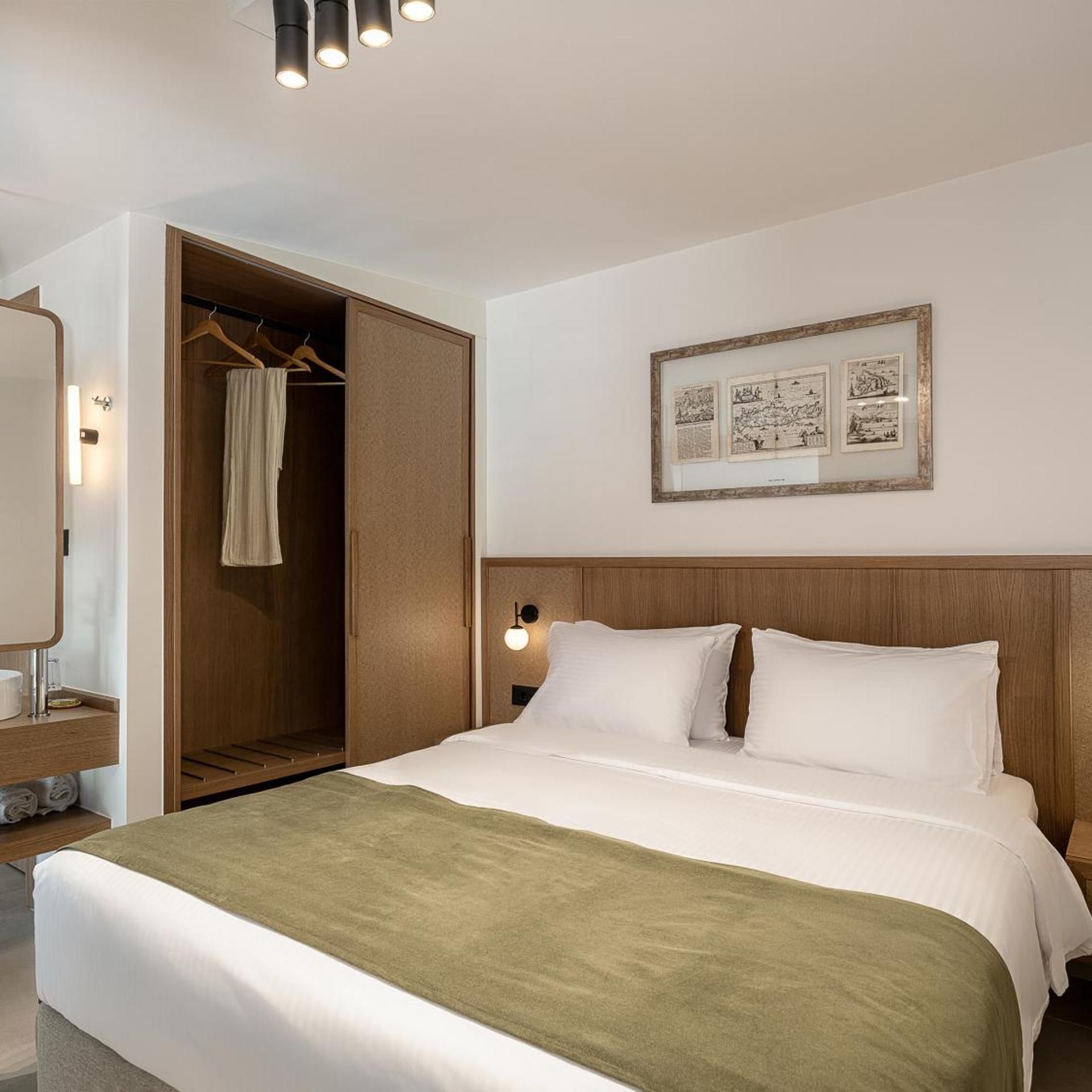 Una habitación de hotel con cama, armario, espejo y un cuadro en la pared.