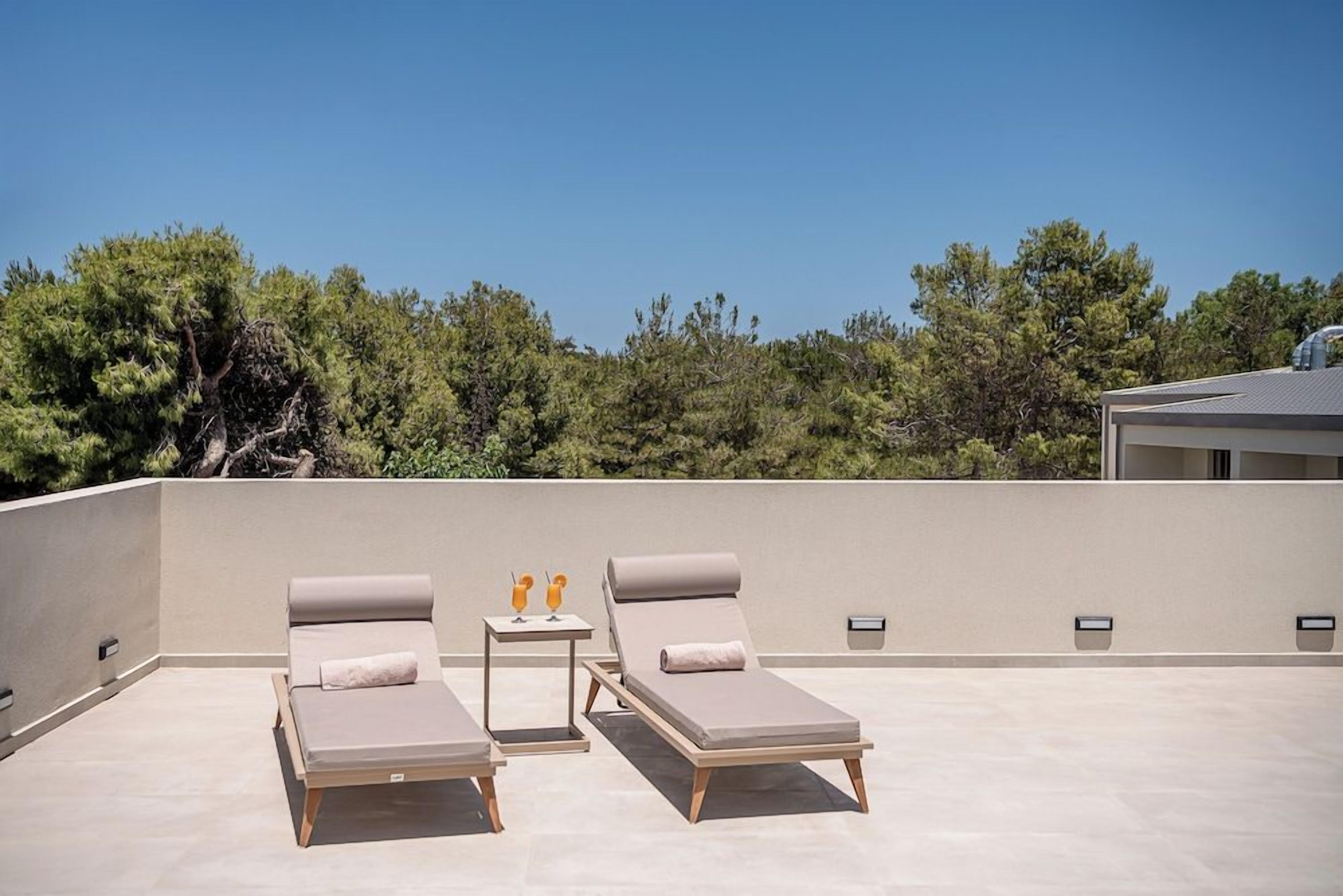 Une terrasse sur le toit avec deux chaises longues, une petite table avec des boissons et une vue dégagée sur les arbres.
