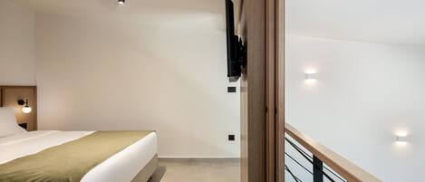 Une chambre d’hôtel moderne équipée d’un lit, d’une tête de lit en bois, d’un téléviseur à écran plat fixé au mur et d’un balcon doté d’une balustrade en bois.